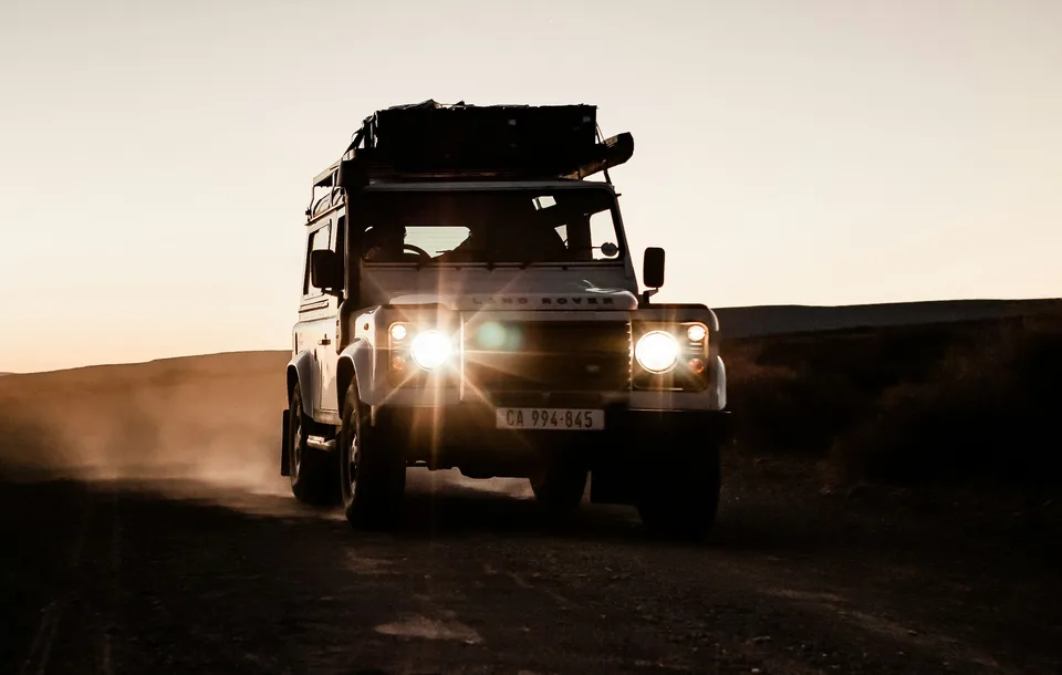 An off-road vehicle with headlights on a dirt road at sunset