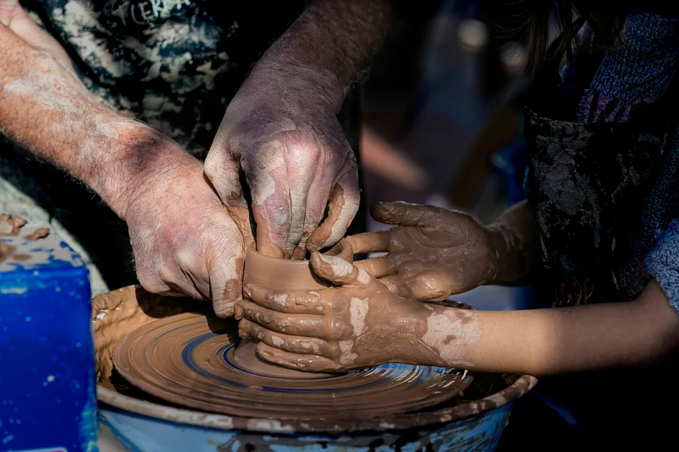 A master guiding a child's hands at the pottery wheel