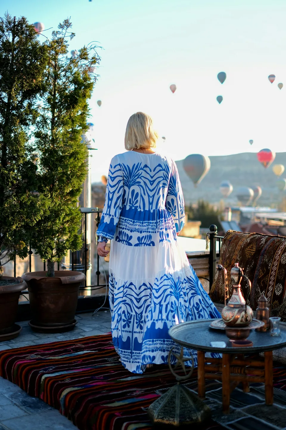 A woman in a long dress on a terrace with balloons in the sky