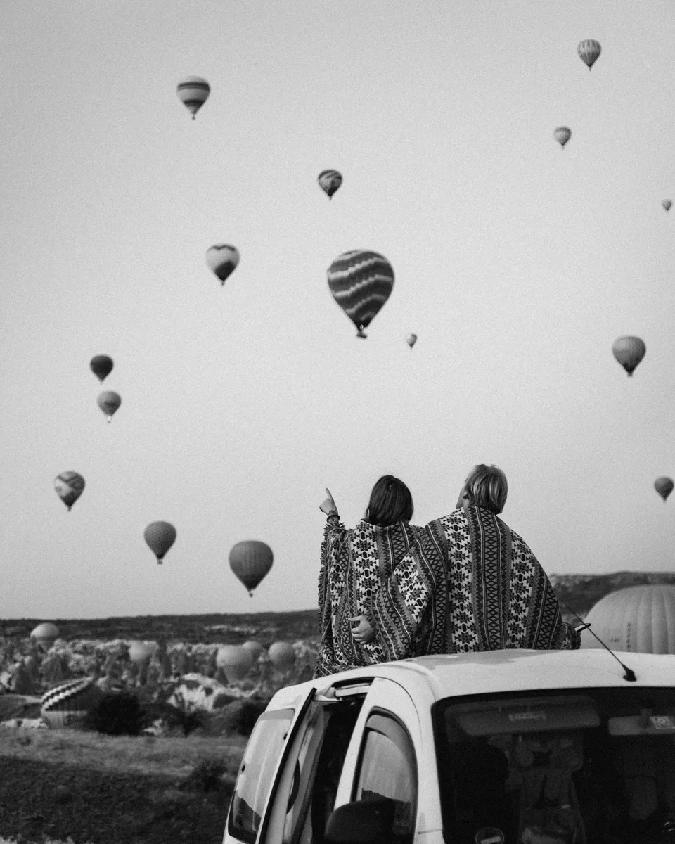 Two people watching the balloons, black and white